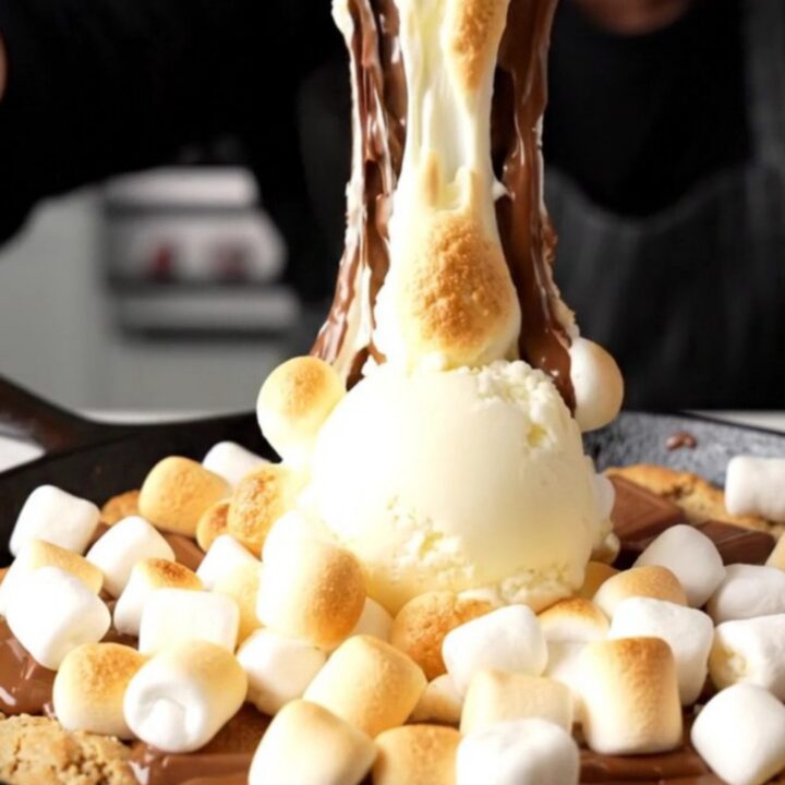 Giant s'mores skillet cookie with golden toasted marshmallows and melted chocolate in a cast iron skillet