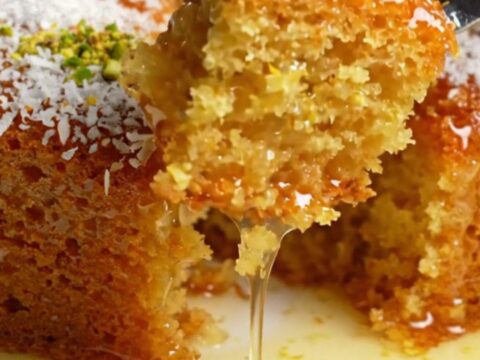 Turkish Revani cake in a baking dish, topped with coconut and pistachios, with syrup pooling around a piece