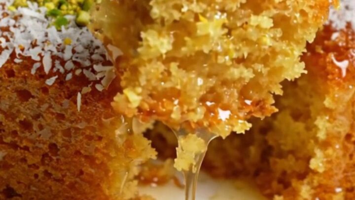 Turkish Revani cake in a baking dish, topped with coconut and pistachios, with syrup pooling around a piece