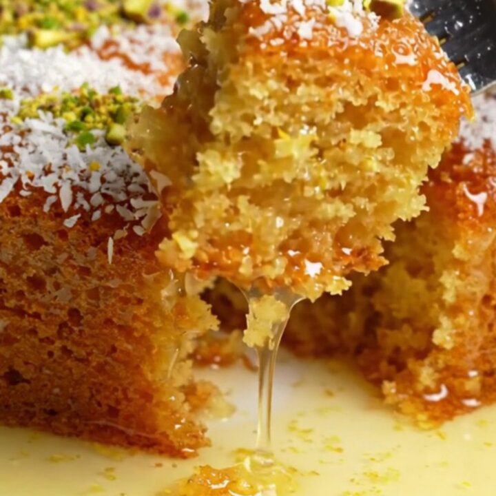 Turkish Revani cake in a baking dish, topped with coconut and pistachios, with syrup pooling around a piece
