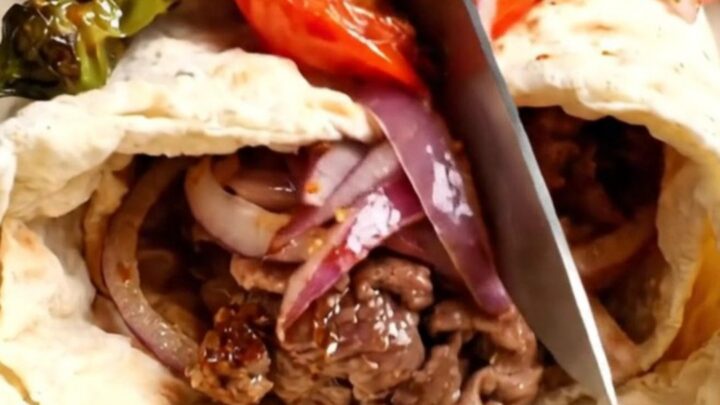 Urfa kebab wrap sliced in half, showing juicy lamb, sumac onions, and charred tomatoes