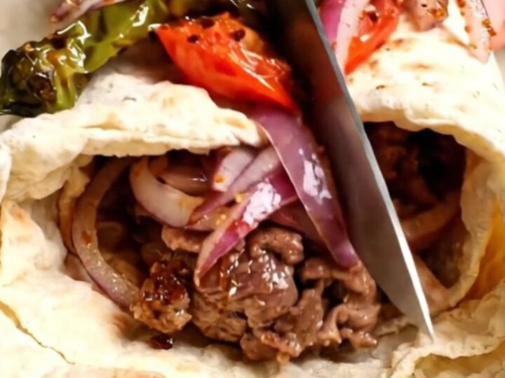 Urfa kebab wrap sliced in half, showing juicy lamb, sumac onions, and charred tomatoes
