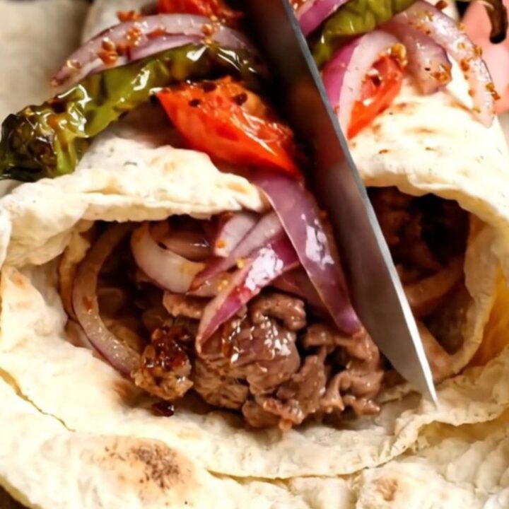 Urfa kebab wrap sliced in half, showing juicy lamb, sumac onions, and charred tomatoes