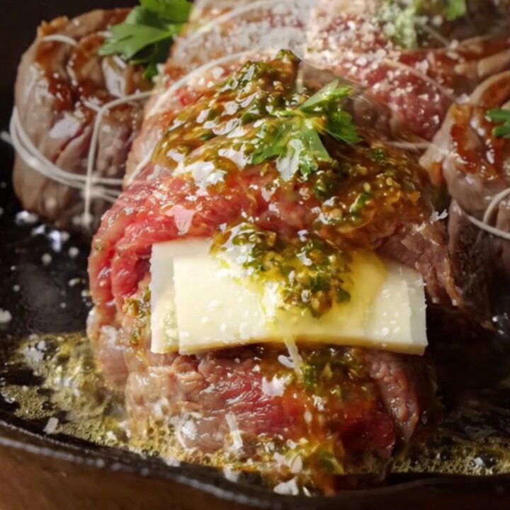 Chimichurri butter flank steak pinwheels seared in a cast-iron skillet, with melted cheese and herb sauce