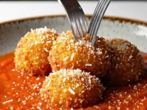 Crispy golden arancini bombs on a plate with marinara sauce and grated pecorino.