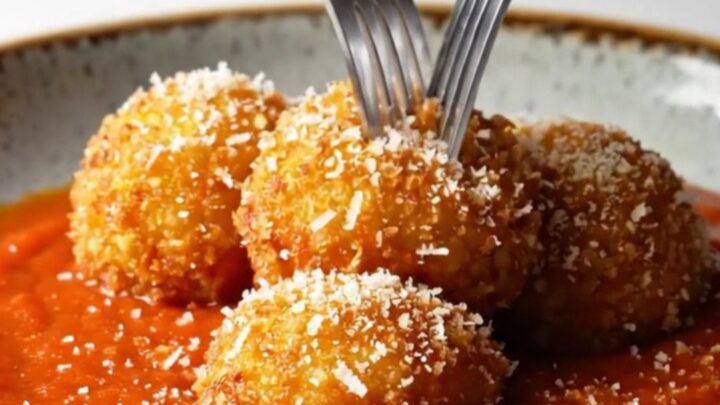 Crispy golden arancini bombs on a plate with marinara sauce and grated pecorino.