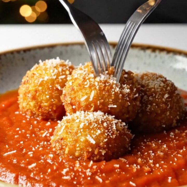 Crispy golden arancini bombs on a plate with marinara sauce and grated pecorino.