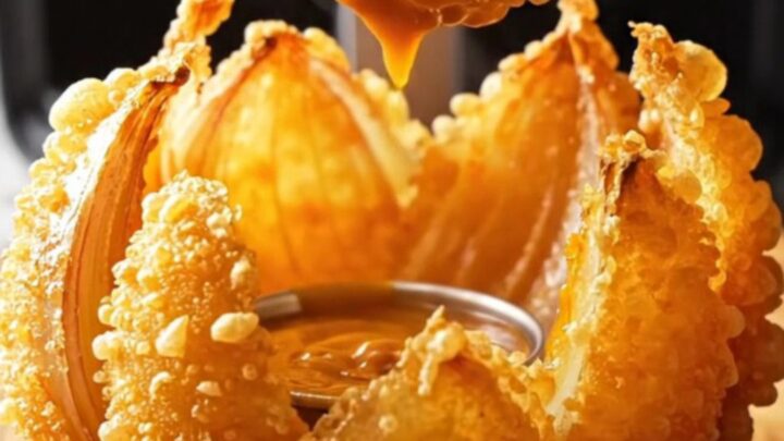 Golden air-fried blooming onion with comeback dip in the center on a wooden board