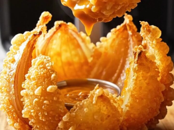 Golden air-fried blooming onion with comeback dip in the center on a wooden board