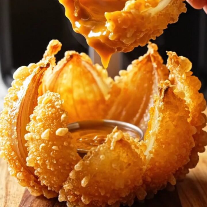 Golden air-fried blooming onion with comeback dip in the center on a wooden board