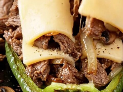Bubbling provolone-topped stuffed bell peppers in a baking dish, with golden cheese and juicy steak filling visible.