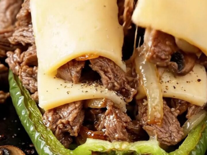 Bubbling provolone-topped stuffed bell peppers in a baking dish, with golden cheese and juicy steak filling visible.