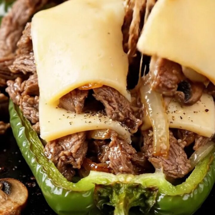 Bubbling provolone-topped stuffed bell peppers in a baking dish, with golden cheese and juicy steak filling visible.