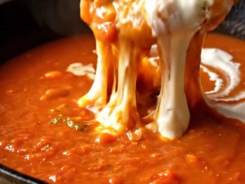 A bowl of roasted garlic tomato bisque with a grilled Gruyère sourdough dipper being dunked into the soup.
