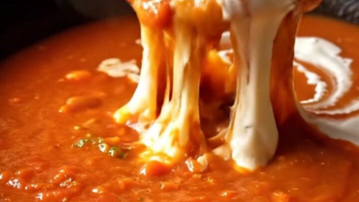A bowl of roasted garlic tomato bisque with a grilled Gruyère sourdough dipper being dunked into the soup.