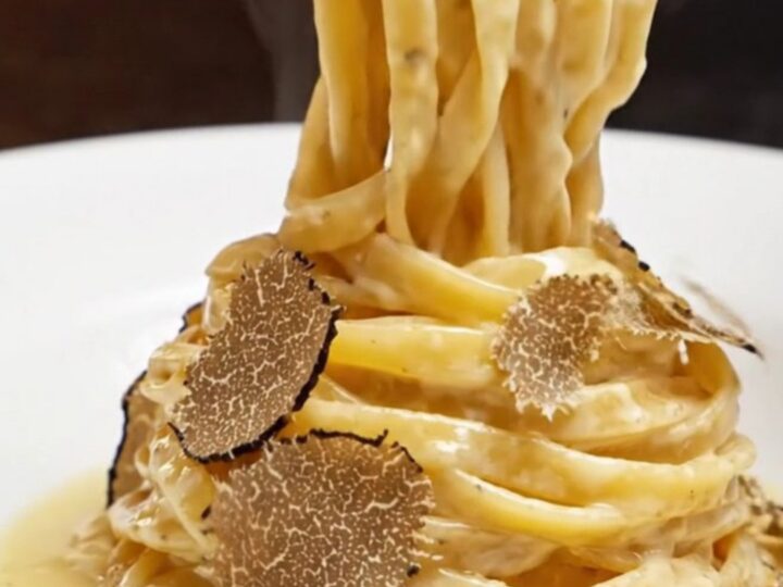 Twirl of fresh fettuccine in a hollowed Grana Padano wheel with melted cheese and truffle shavings