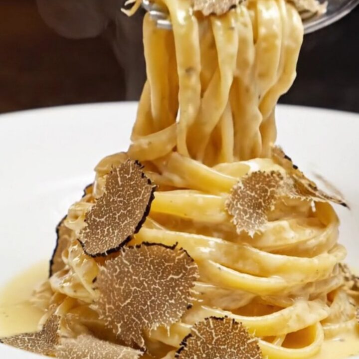 Twirl of fresh fettuccine in a hollowed Grana Padano wheel with melted cheese and truffle shavings