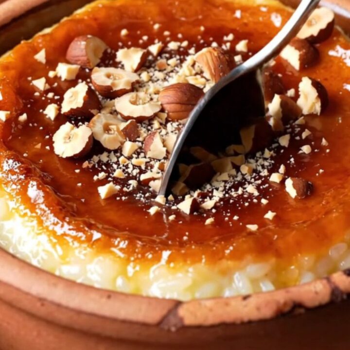 Caramelized Turkish baked rice pudding in a clay bowl with a blistered brown top and crushed hazelnuts