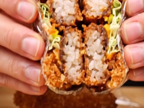 Cross-section of a crispy tonkatsu onigirazu showing layers of rice, cabbage, katsu, and sauce.