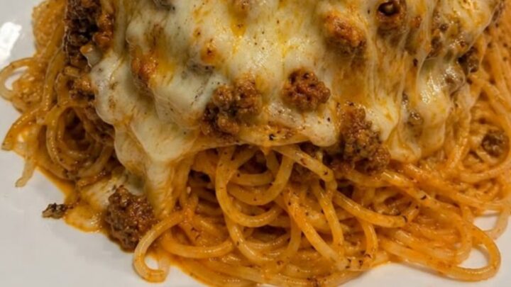 A fork lifting a large portion of spaghetti with a long, gooey cheese pull from a mound of meat-sauce-covered pasta.