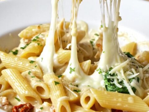 Skillet scoop lifting creamy Tuscan chicken pasta with melted mozzarella and sun-dried tomatoes