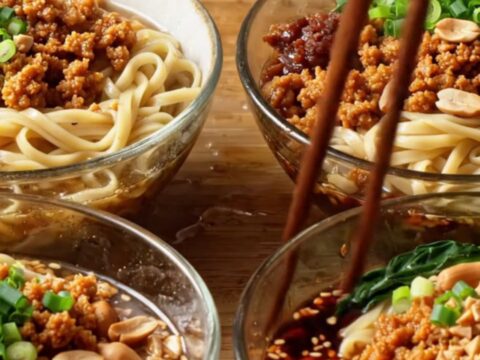A bowl of Szechuan Dan Dan Noodles topped with crispy pork, crushed peanuts, and green bok choy