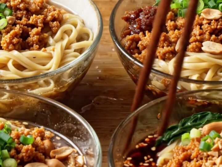 A bowl of Szechuan Dan Dan Noodles topped with crispy pork, crushed peanuts, and green bok choy