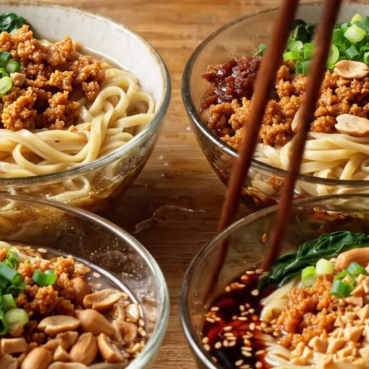 A bowl of Szechuan Dan Dan Noodles topped with crispy pork, crushed peanuts, and green bok choy