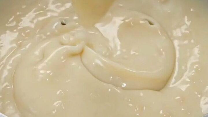 A silver pot filled with glossy, thick coconut cream with a spatula lifting a ribbon of the pudding.