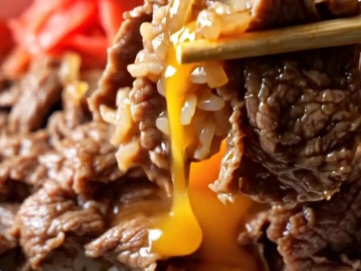 A bowl of gyudon with shaved beef, onions, and a soft-poached egg over rice.