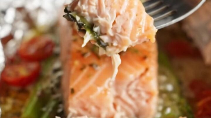 A foil packet opened to reveal a salmon fillet with asparagus and cherry tomatoes in garlic butter sauce.