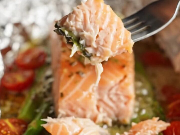 A foil packet opened to reveal a salmon fillet with asparagus and cherry tomatoes in garlic butter sauce.