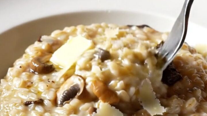 A wide shallow plate of creamy wild mushroom risotto swirled with truffle oil and topped with shaved Grana Padano