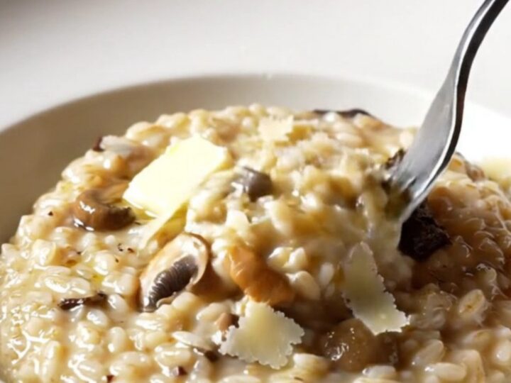 A wide shallow plate of creamy wild mushroom risotto swirled with truffle oil and topped with shaved Grana Padano