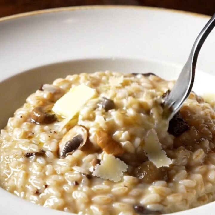 A wide shallow plate of creamy wild mushroom risotto swirled with truffle oil and topped with shaved Grana Padano