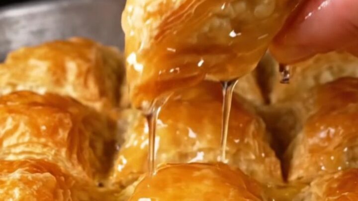 Triangle of golden baklava with green pistachio filling, syrup glaze on a plate