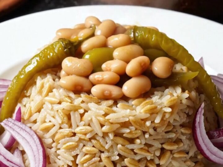 A clay pot of Turkish kuru fasulye with tender veal and white beans in a rich red sauce, served over buttered rice pilaf.