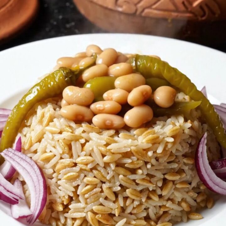 A clay pot of Turkish kuru fasulye with tender veal and white beans in a rich red sauce, served over buttered rice pilaf.