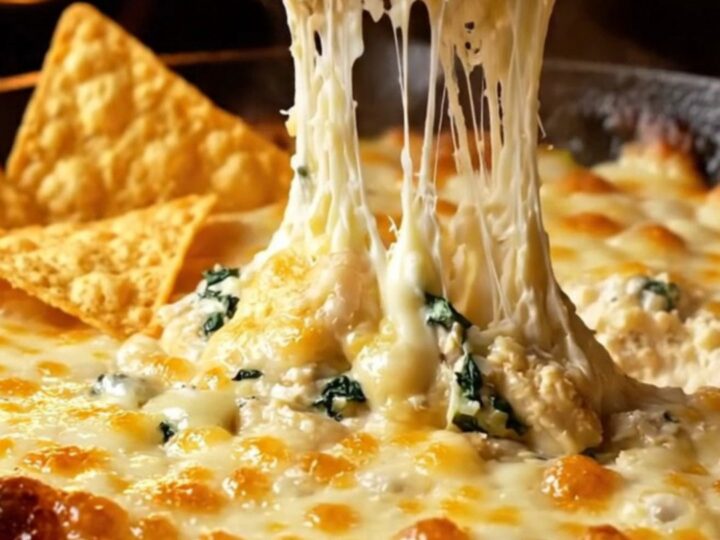 Creamy spinach artichoke dip in a cast-iron skillet with a tortilla chip scooping up melted cheese.
