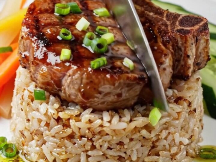 Charcoal-grilled lemongrass pork chop on a plate with broken rice, pickled carrots, and cucumber
