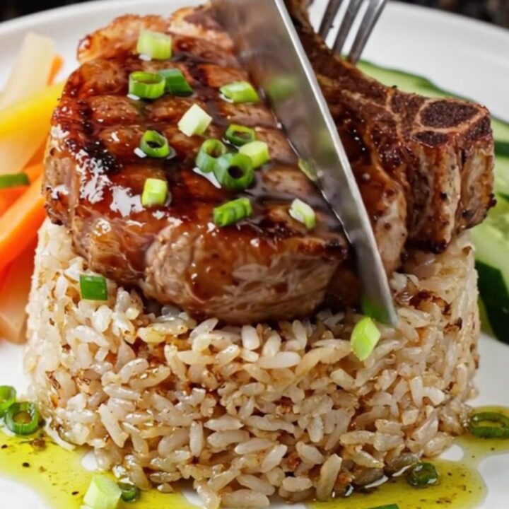 Charcoal-grilled lemongrass pork chop on a plate with broken rice, pickled carrots, and cucumber