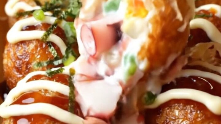 Golden crispy takoyaki balls topped with takoyaki sauce, Kewpie mayo, aonori, and dancing bonito flakes on a wooden plate.