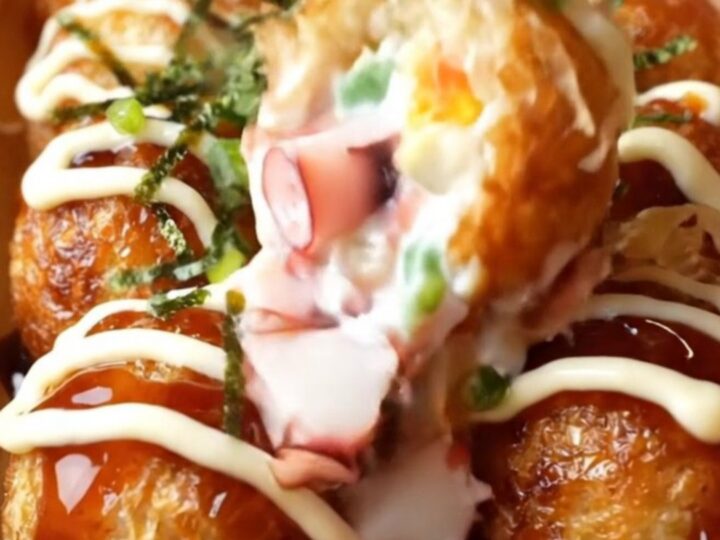 Golden crispy takoyaki balls topped with takoyaki sauce, Kewpie mayo, aonori, and dancing bonito flakes on a wooden plate.