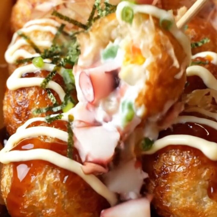 Golden crispy takoyaki balls topped with takoyaki sauce, Kewpie mayo, aonori, and dancing bonito flakes on a wooden plate.