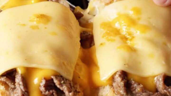 Loaded Philly cheesesteak garlic bread boats with melted provolone, sliced diagonally, showing layers of steak, onions