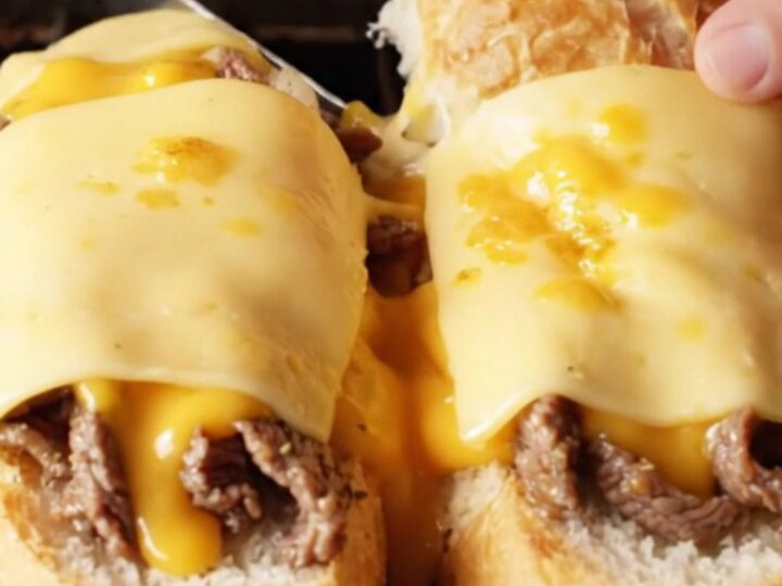 Loaded Philly cheesesteak garlic bread boats with melted provolone, sliced diagonally, showing layers of steak, onions