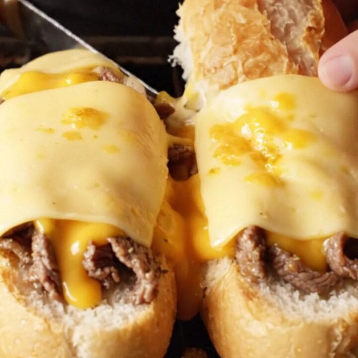 Loaded Philly cheesesteak garlic bread boats with melted provolone, sliced diagonally, showing layers of steak, onions