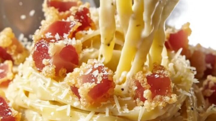 A fork twirling creamy truffle fettuccine carbonara topped with crispy guanciale cubes