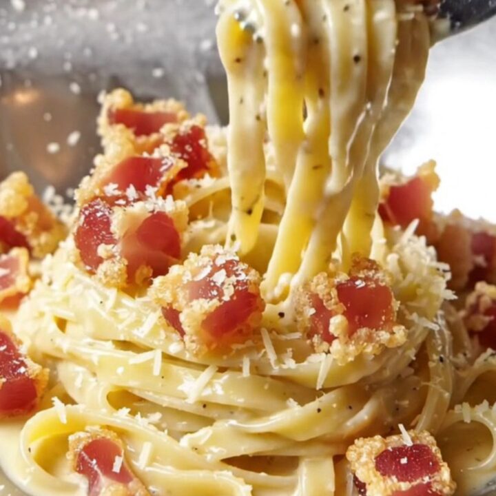 A fork twirling creamy truffle fettuccine carbonara topped with crispy guanciale cubes