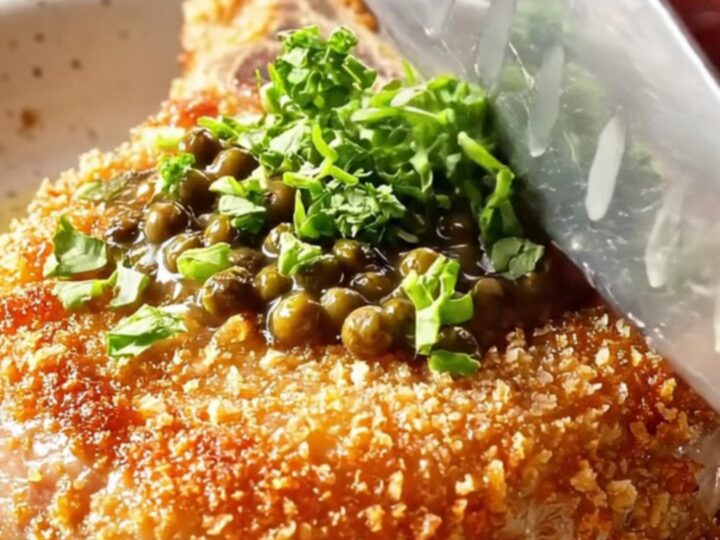 Crispy fried pork chop with creamy peppercorn sauce spooned over, garnished with parsley.